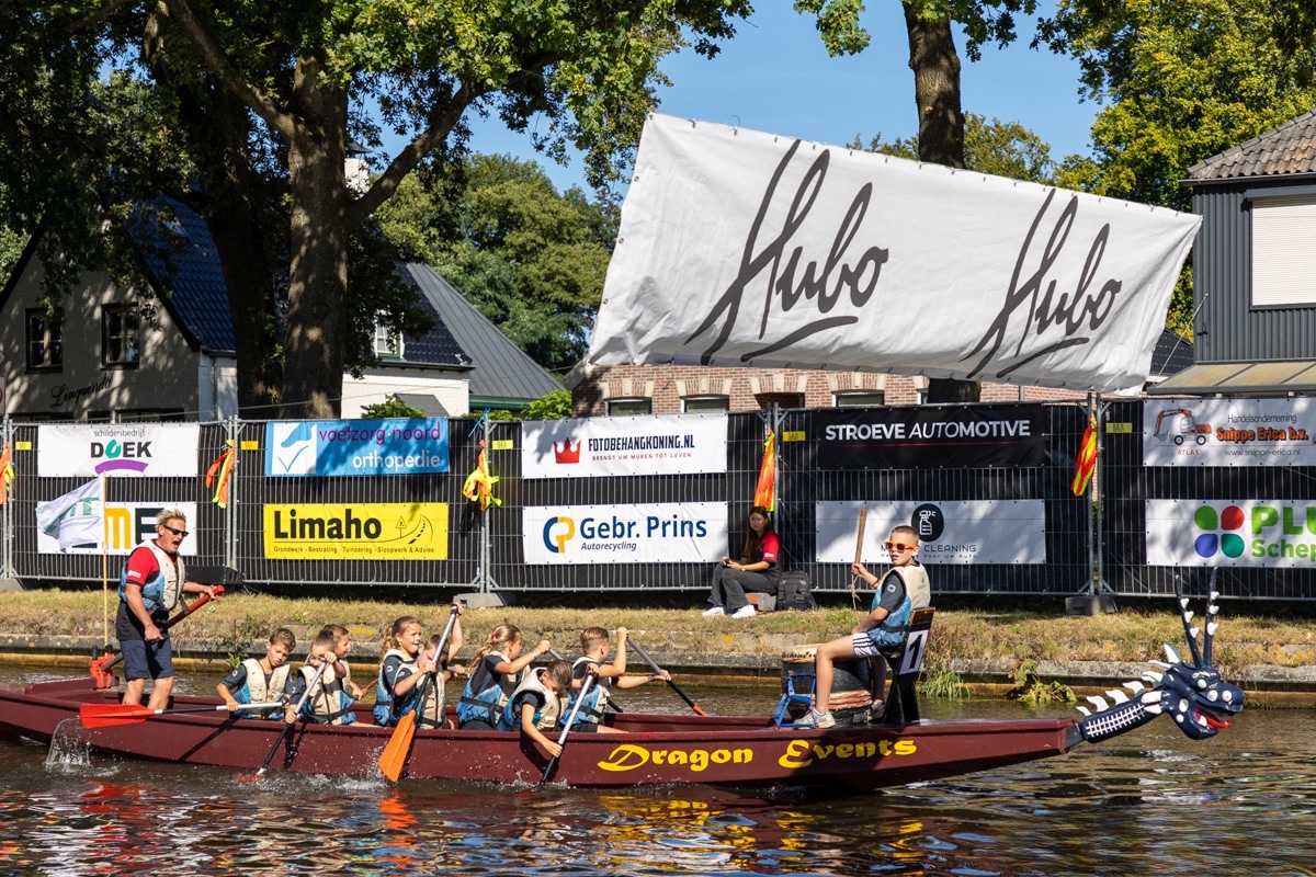 Drakenboot op het water met sponsorbanners langs de wedstrijdbaan